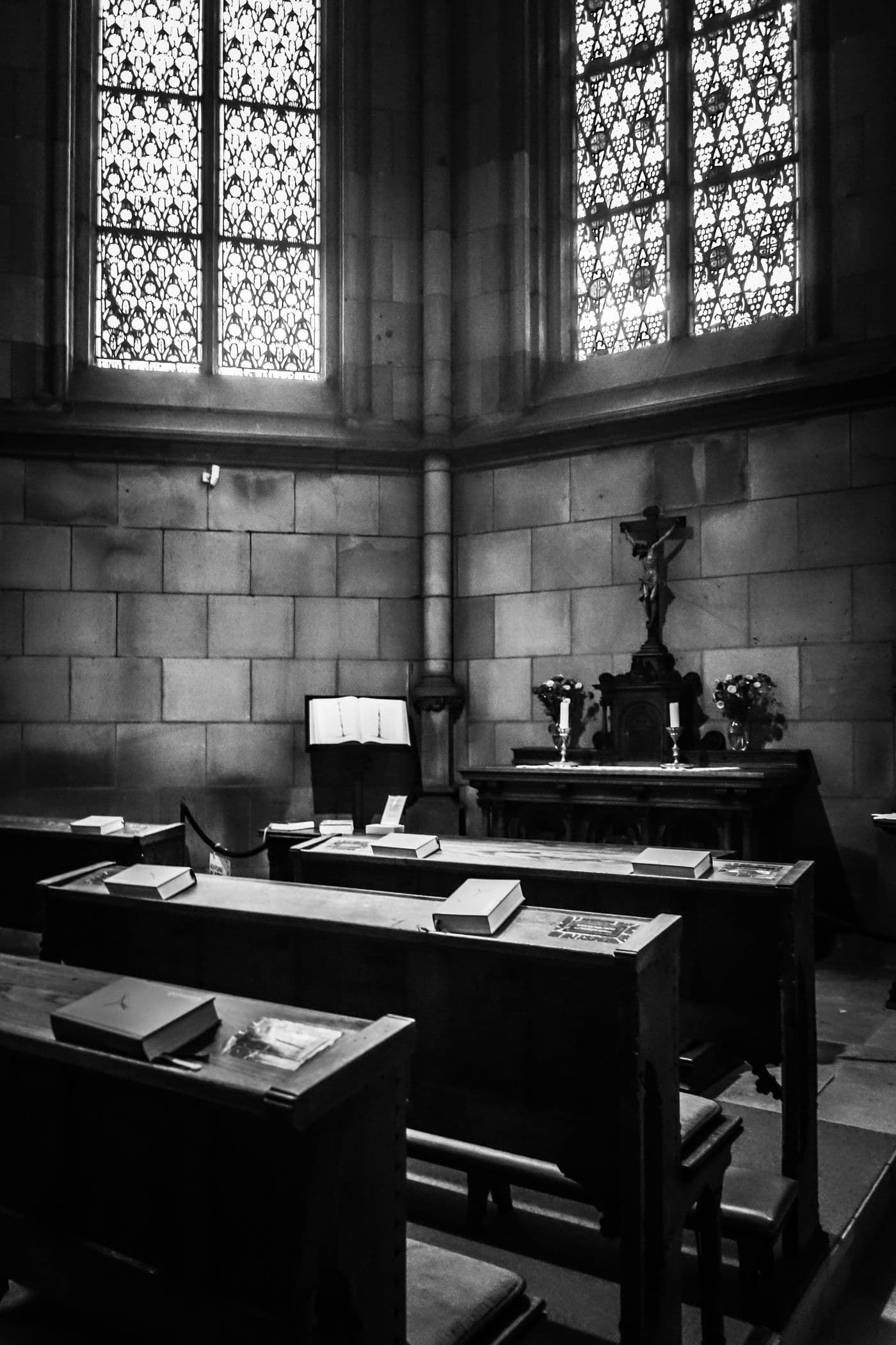 Black and white photograph of wooden desks with books in a stone hall